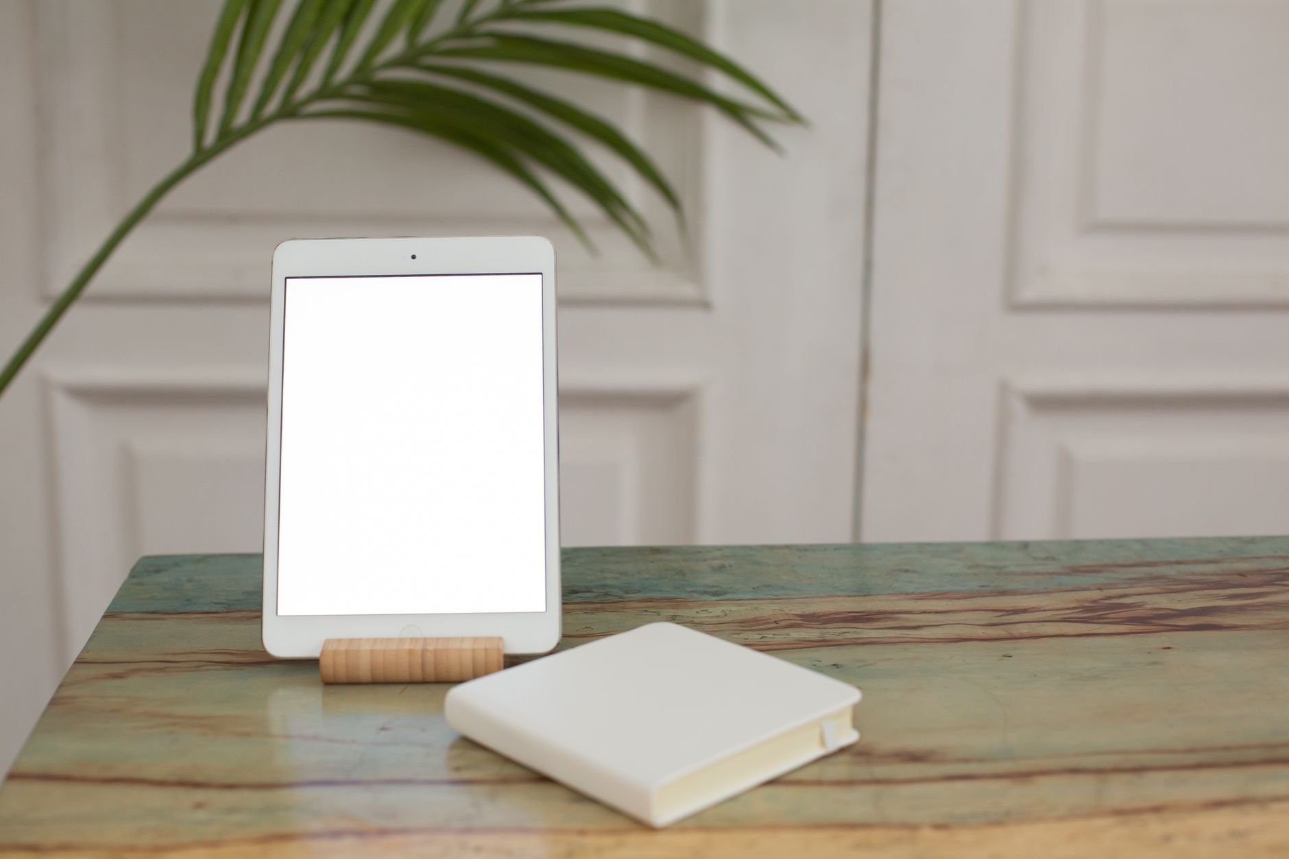 A digital tablet with a blank screen and a closed notebook on a wooden table indoors.